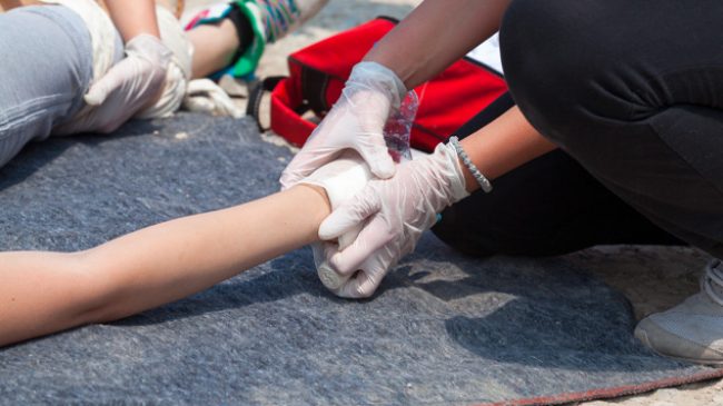 Cursist verbindt de arm van een slachtoffer tijdens een EHBO-oefening