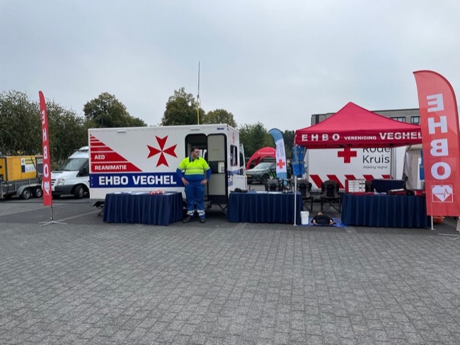 Hulpverlener bij de EHBO-stand met materiaalwagen en tent van EHBO Veghel